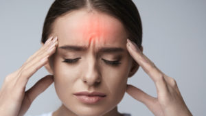 Photograph of woman with headache rubbing temples with eyes closed